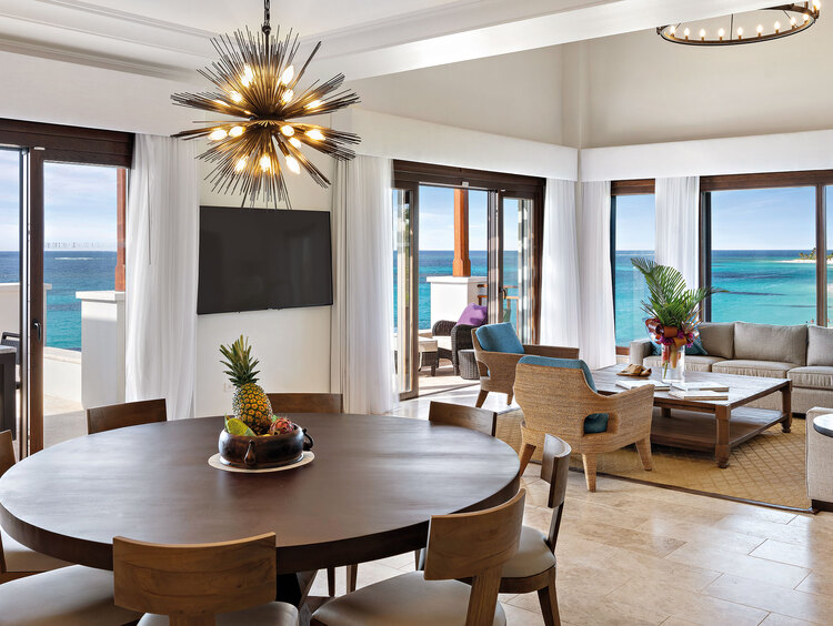Tavolo marrone con sedie accanto al soggiorno con TV e vista sull'oceano dal balcone