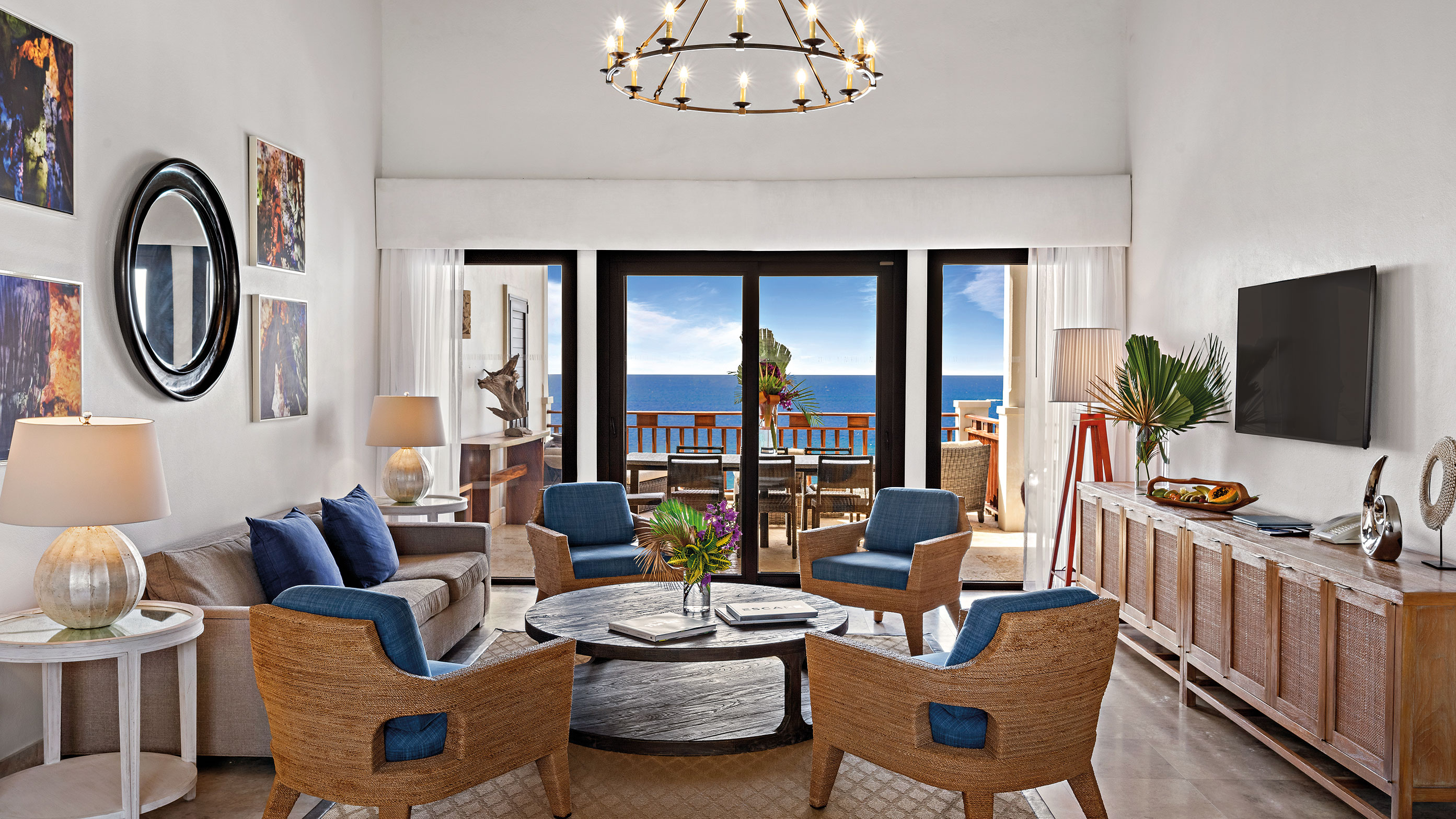 Sala de estar com mesa e cadeiras, TV e vista para o mar da varanda